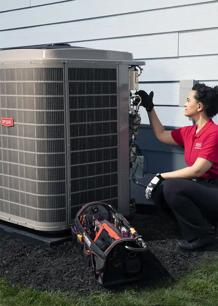 HVAC Technician servicing a heat pump unit outside with tool bag | Bennett Heating and Air LLC