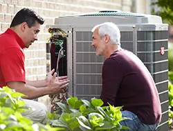 Heat Pump Repair Technician crouching with homeowner near heat pump's outdoor unit | Bennett Heating and Air LLC